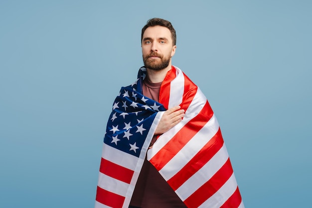 Uomo sicuro e serio che copre la bandiera americana isolato su uno sfondo blu