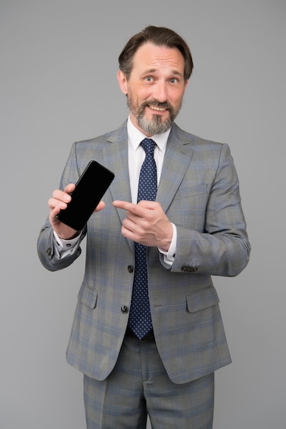 Uomo sicuro in abbigliamento casual intelligente tenere lo smartphone puntando il dito sul dispositivo digitale esperto di social network nel marketing digitale maturo direttore generale maschio dirigente d'azienda