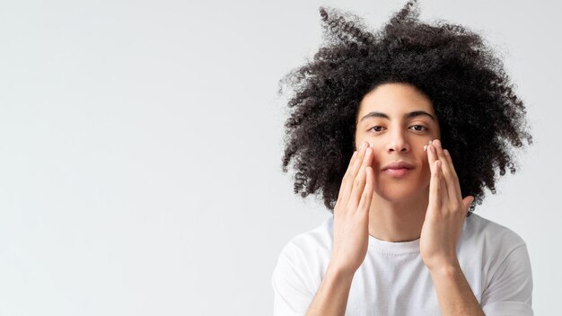 Uomo skincare trattamento viso pelle idratante fiducioso bel ragazzo con lunghi capelli ricci castani dentro