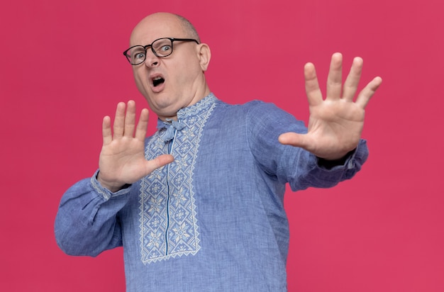 Uomo slavo adulto scontento in camicia blu che indossa occhiali ottici allungando le mani e guardando di lato