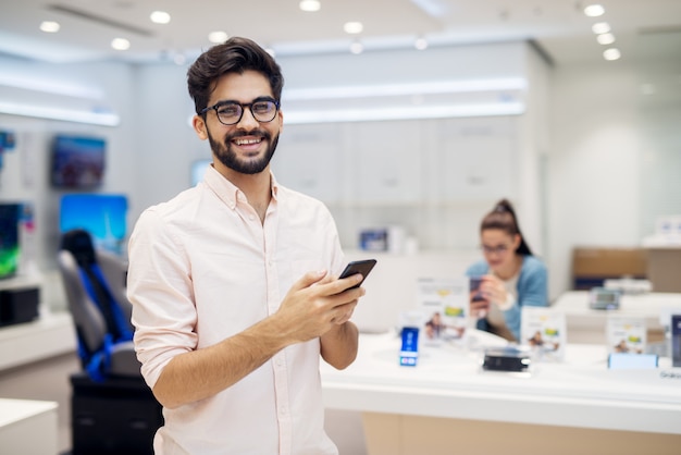 Uomo soddisfatto affascinante alla moda soddisfatto giovane che tiene il nuovo modello di cellulare dal negozio di tecnologia.