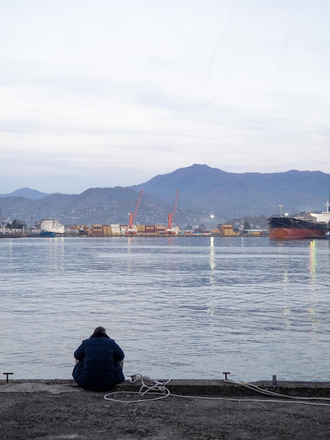 uomo solitario si siede sul molo la sera un uomo è seduto nella zona del porto concetto di solitudine città portuale in inverno