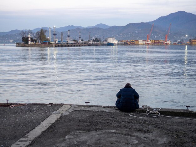 uomo solitario si siede sul molo la sera un uomo è seduto nella zona del porto concetto di solitudine città portuale in inverno