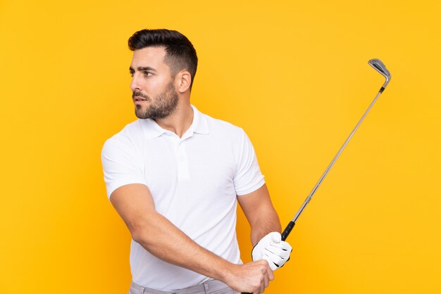 Uomo sopra la parete gialla isolata che gioca golf