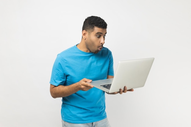 Uomo sorpreso in piedi che tiene il portatile nelle mani lavorando online guardando lo schermo con grandi occhi