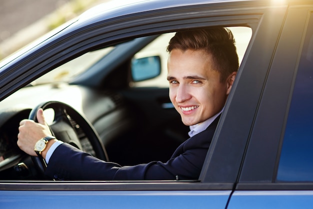 Uomo sorridente bello attraente in un vestito che conduce un'automobile costosa