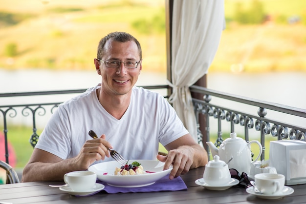 Uomo sorridente bello in caffè che mangia il dolce Pavlova