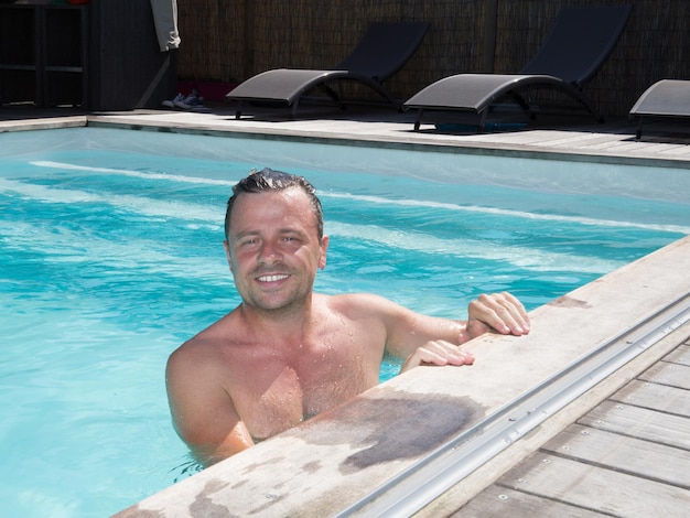 Uomo sorridente bello in piscina nel paesaggio di vacanza di vacanze estive