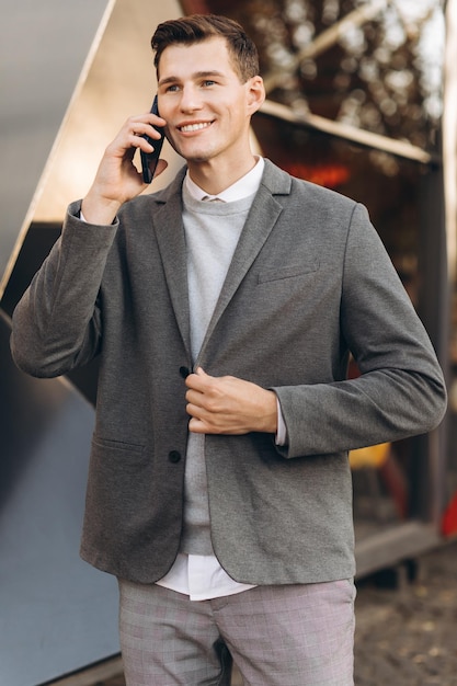 Uomo sorridente bello moderno che cammina per strada e parla al telefono