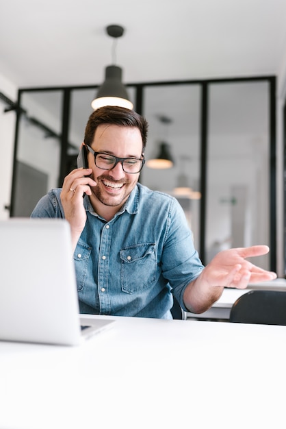 Uomo sorridente che comunica sul telefono al lavoro all&#39;interno.