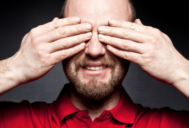 uomo sorridente che copre gli occhi con le mani