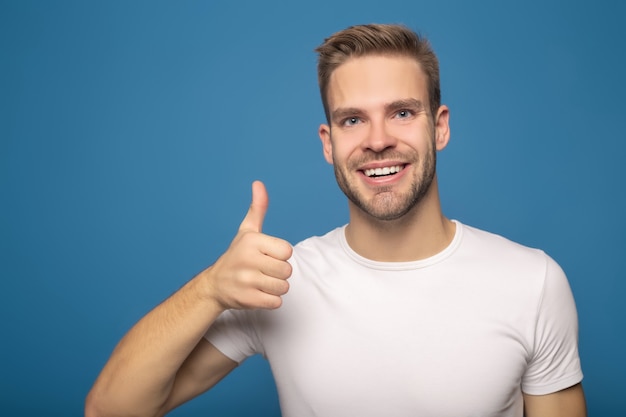 uomo sorridente che mostra pollice in su isolato sull'azzurro