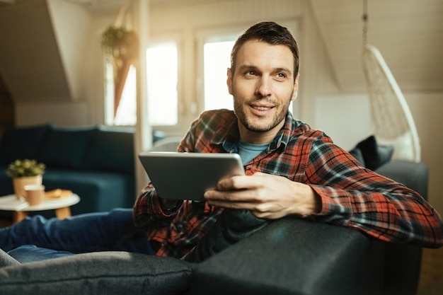 Uomo sorridente che naviga in rete sul touchpad mentre si riposa nel soggiorno