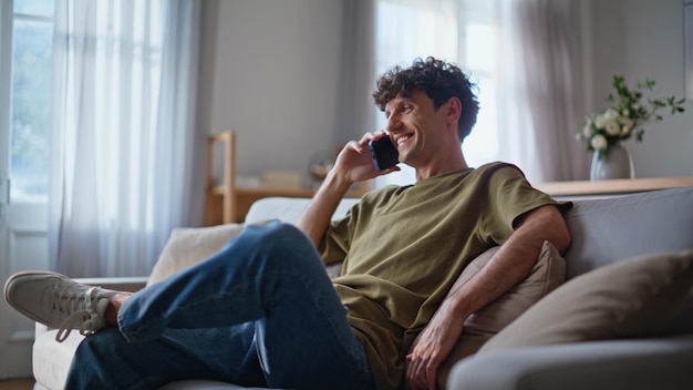 Uomo sorridente che parla al cellulare sul divano del soggiorno, primo piano.
