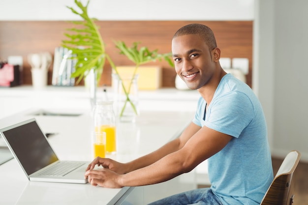 Uomo sorridente che per mezzo del computer portatile a casa