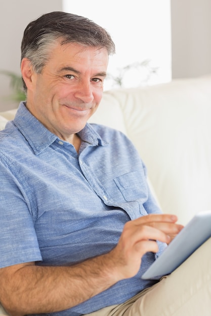 Uomo sorridente che si siede su un divano con un tablet pc