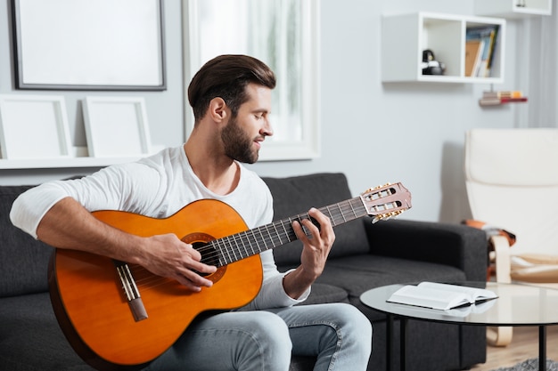 Uomo sorridente che si siede sul sofà che gioca sulla chitarra