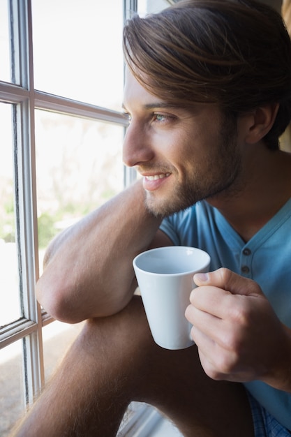 Uomo sorridente che si siede vicino alla finestra che mangia caffè