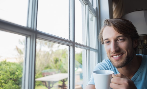 Uomo sorridente che si siede vicino alla finestra che mangia caffè