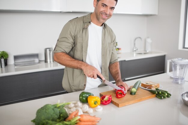 Uomo sorridente che taglia le verdure a pezzi in cucina