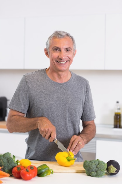 Uomo sorridente che taglia un peperone giallo