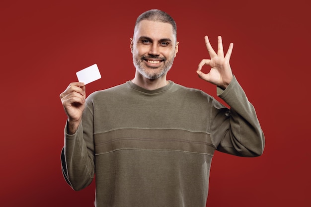 Uomo sorridente che tiene una carta bianca e fa il segno OK