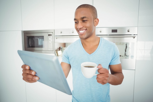 Uomo sorridente che utilizza compressa e che tiene caffè nella cucina