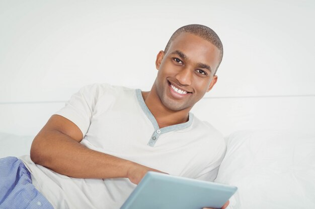 Uomo sorridente che utilizza compressa sul letto