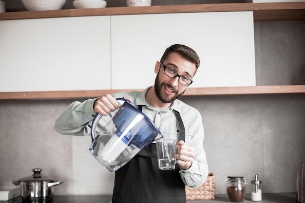 Uomo sorridente che versa acqua pulita in un bicchiere