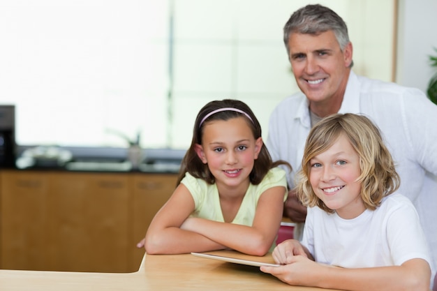 Uomo sorridente con bambini e tablet in cucina