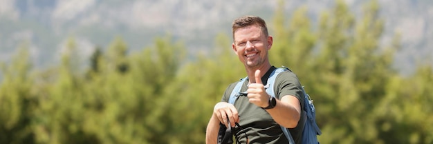 Uomo sorridente con bastoni da passeggio scandinavi e mostrando il segno del pollice in su