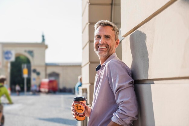 Uomo sorridente con caffè da asporto in città