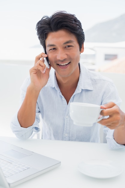 Uomo sorridente con caffè e parlando al telefono