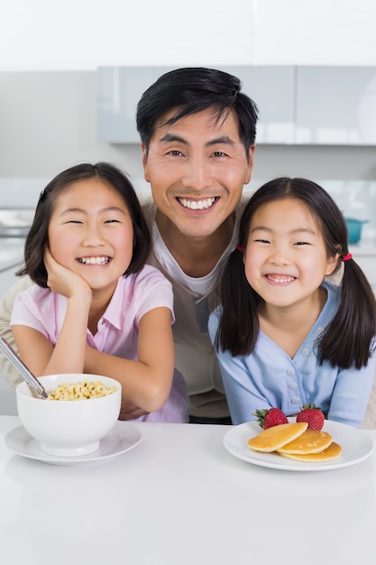 Uomo sorridente con due figlie facendo colazione in cucina