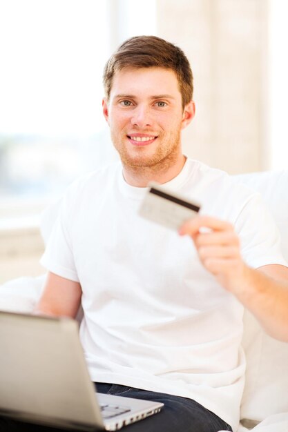 uomo sorridente con il computer portatile che mostra la carta di credito a casa