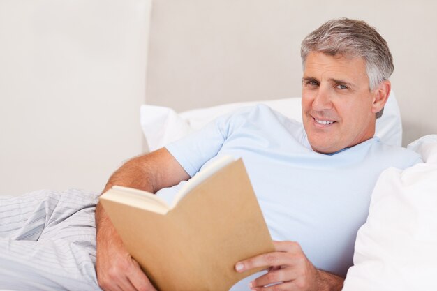 Uomo sorridente con il libro a letto