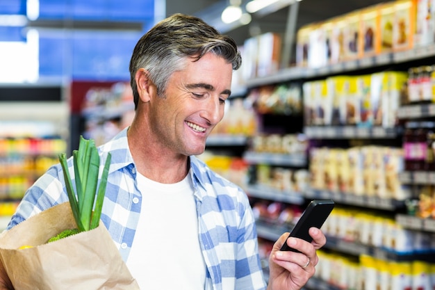 Uomo sorridente con la borsa della spesa tramite smartphone