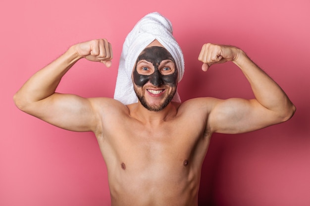 Uomo sorridente con una maschera cosmetica sul viso, nudo mostra i muscoli su uno sfondo rosa.