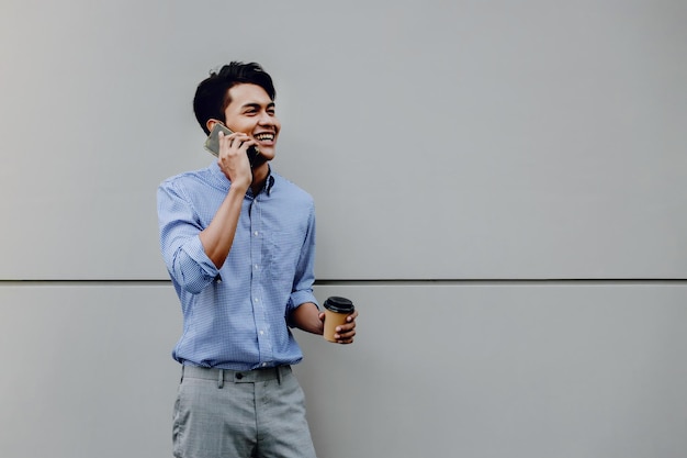 Uomo sorridente con una tazza di caffè che parla al telefono mentre è in piedi contro il muro