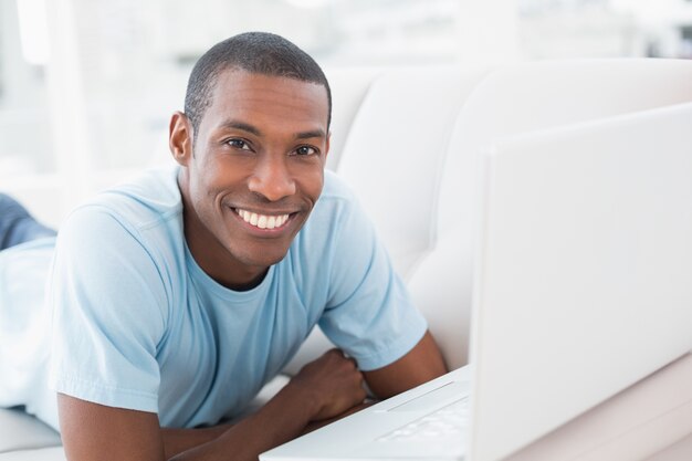 Uomo sorridente di afro con il computer portatile che si trova sul sofà