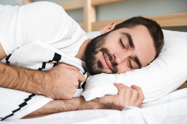 Uomo sorridente di Handsonme che dorme su un cuscino nel letto