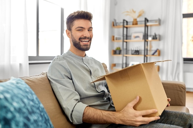 uomo sorridente felice che apre una scatola di pacchi a casa