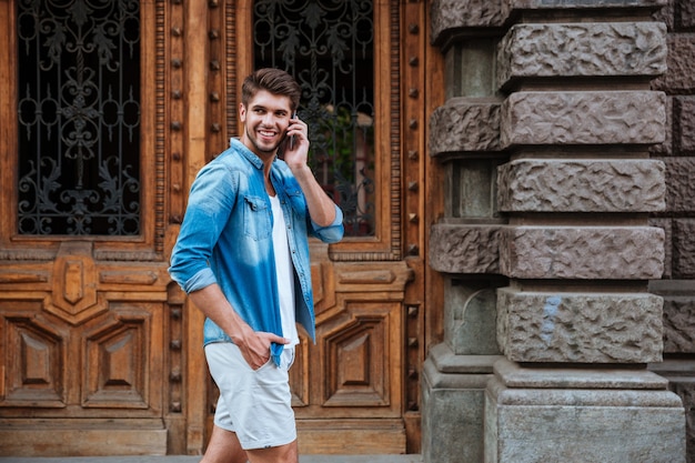 Uomo sorridente felice che parla al telefono cellulare mentre cammina per strada