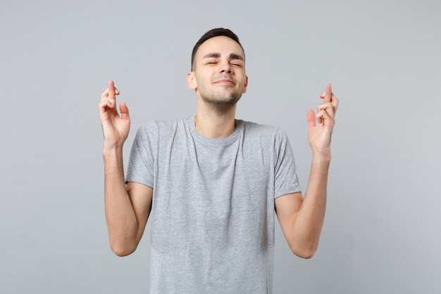 Uomo sorridente in abiti casual in attesa di un momento speciale, tenendo le dita incrociate, gli occhi chiusi, esprimendo un desiderio