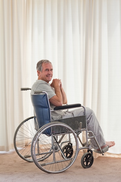 Uomo sorridente nella sua sedia a rotelle a casa