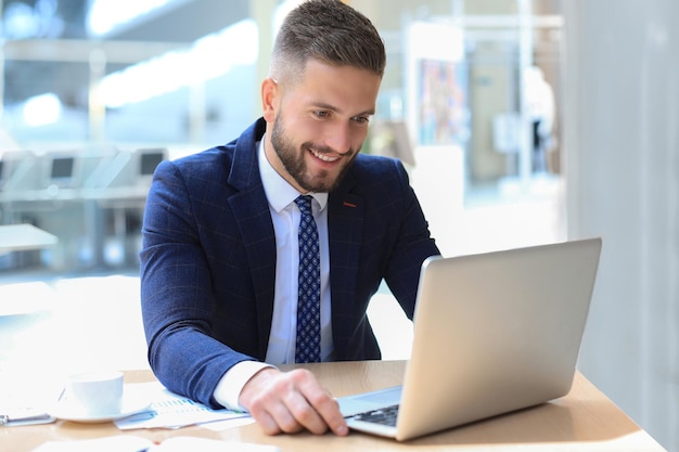 Uomo sorridente seduto in ufficio e usando il suo laptop.