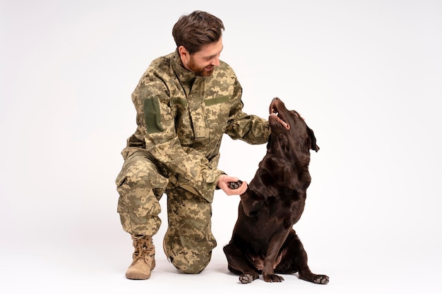 Uomo sorridente soldato che indossa camuffamento militare addestramento cane Labrador isolato su sfondo bianco