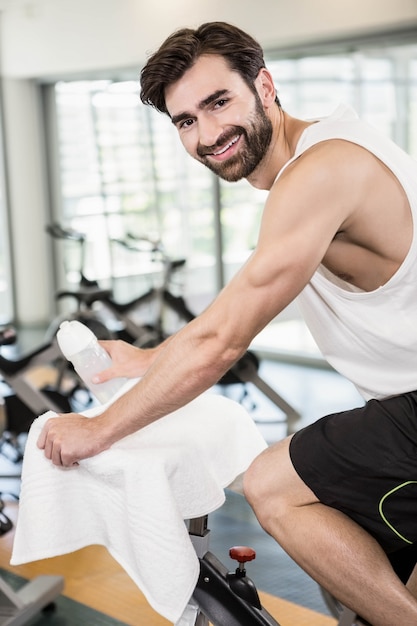 Uomo sorridente sulla bici di esercitazione che esamina la macchina fotografica in palestra