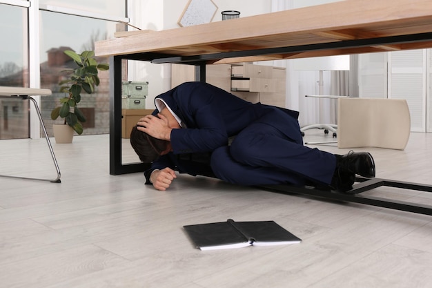 Uomo spaventato che si nasconde sotto la scrivania dell'ufficio durante il terremoto