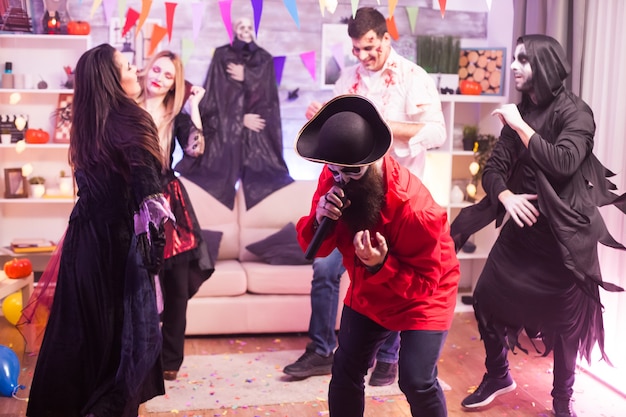 Uomo spettrale vestito come un pirata che fa karaoke alla festa di Halloween per i suoi amici.